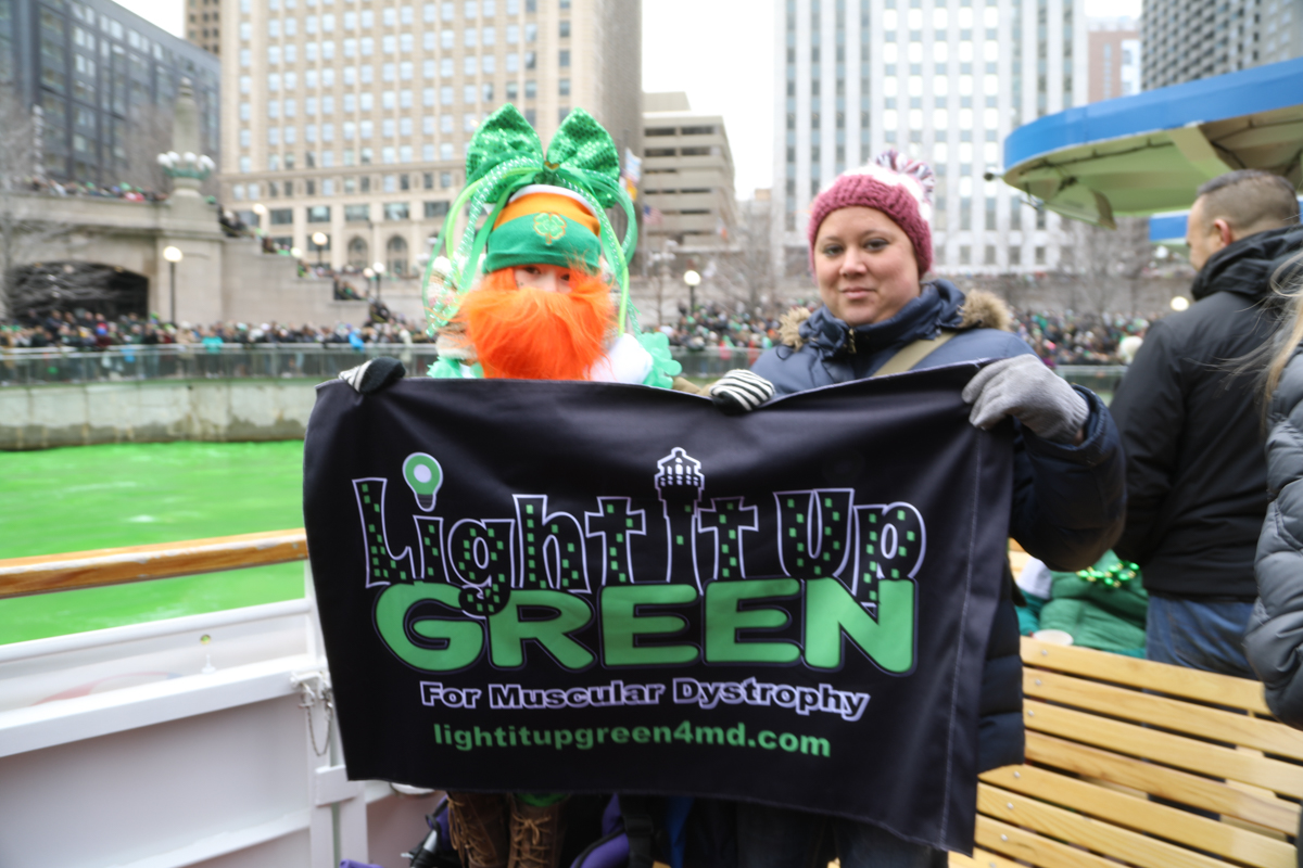 Two people holding up Light it Up Green poster for Chicago St. Patrick's Day parade