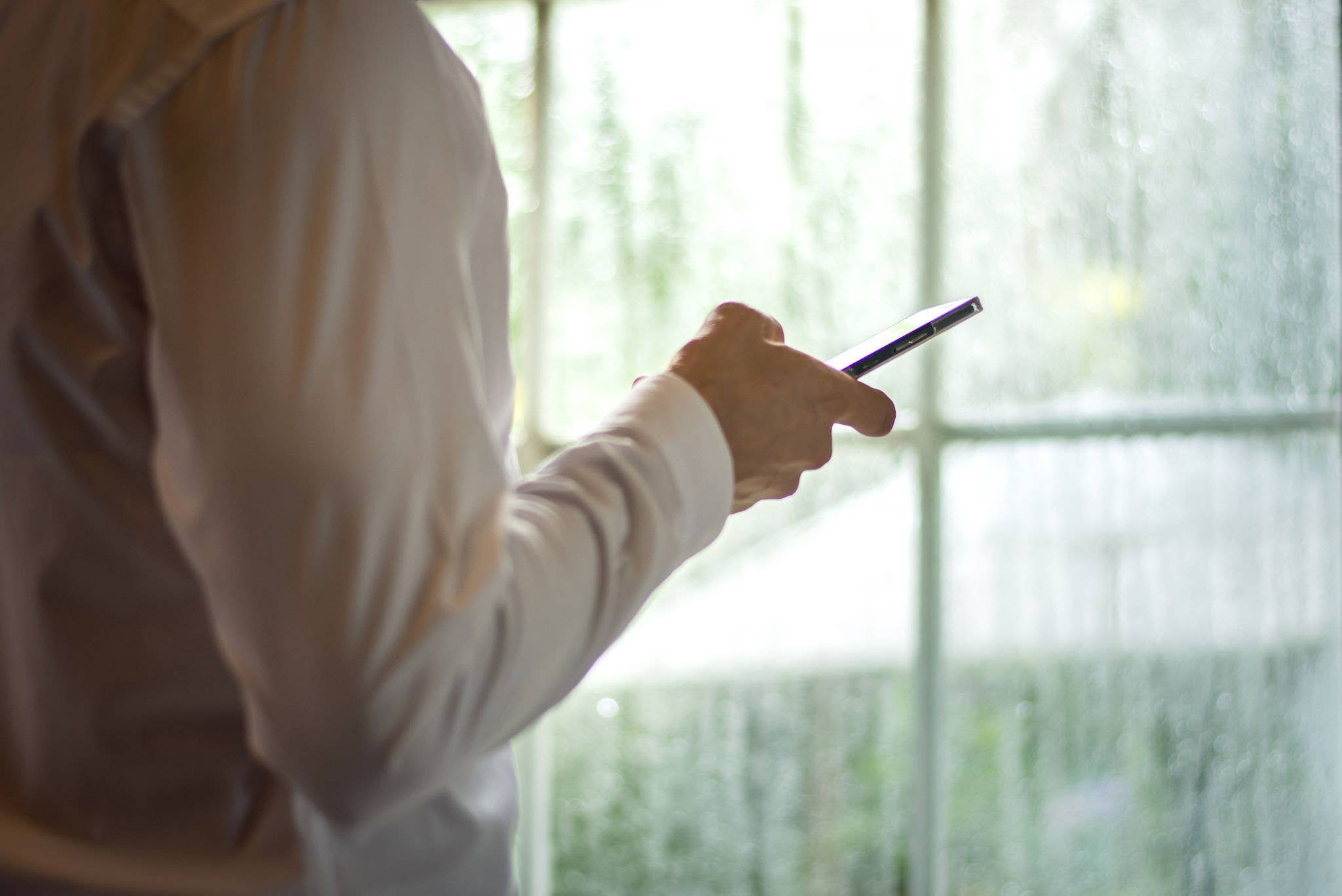 Person looking at phone by window with rain drops
