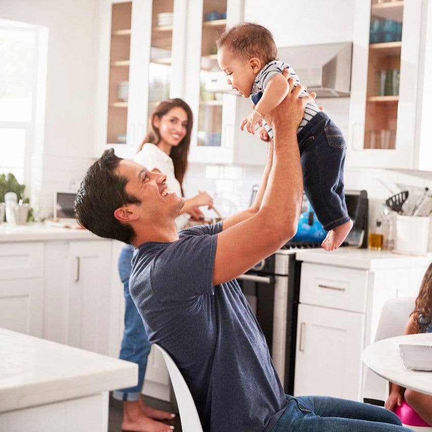 Family in kitchen, dad lifting up baby