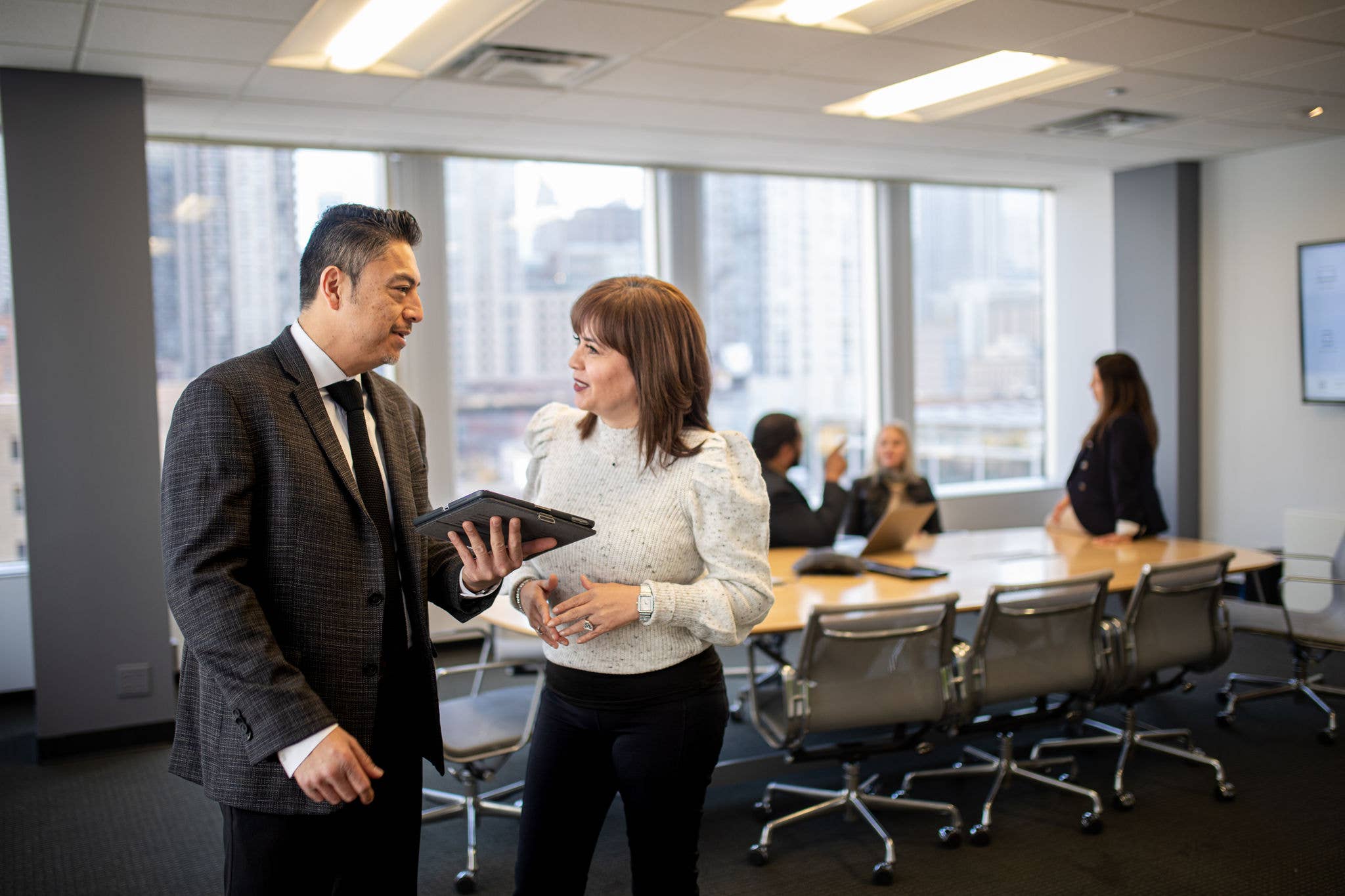 Man holding an iPad talking with a woman in a business meeting room.
