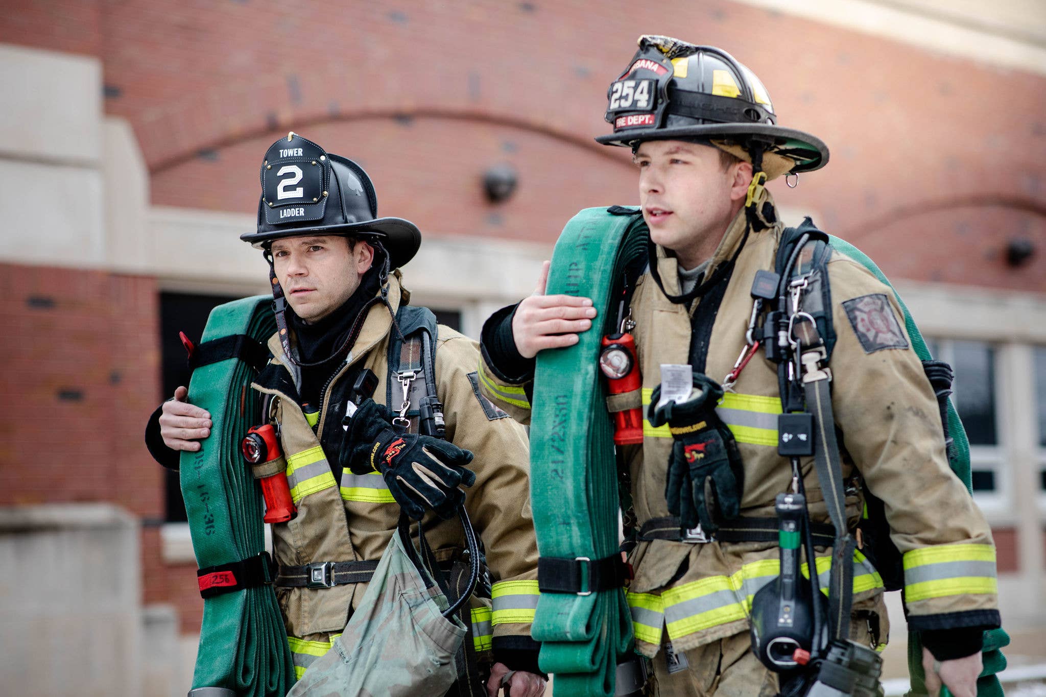 Two firefighters carrying equipment.