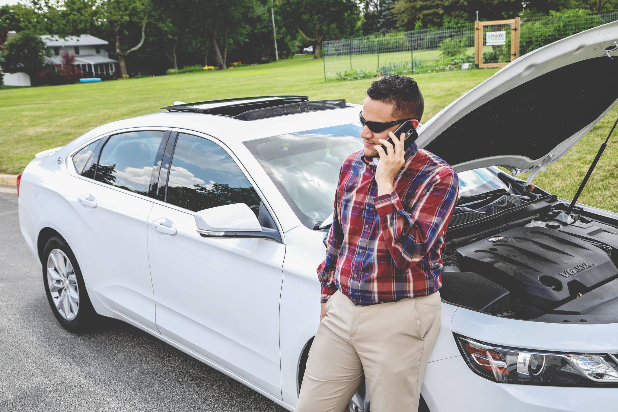 Man on the phone standing outside his car with the hood open.