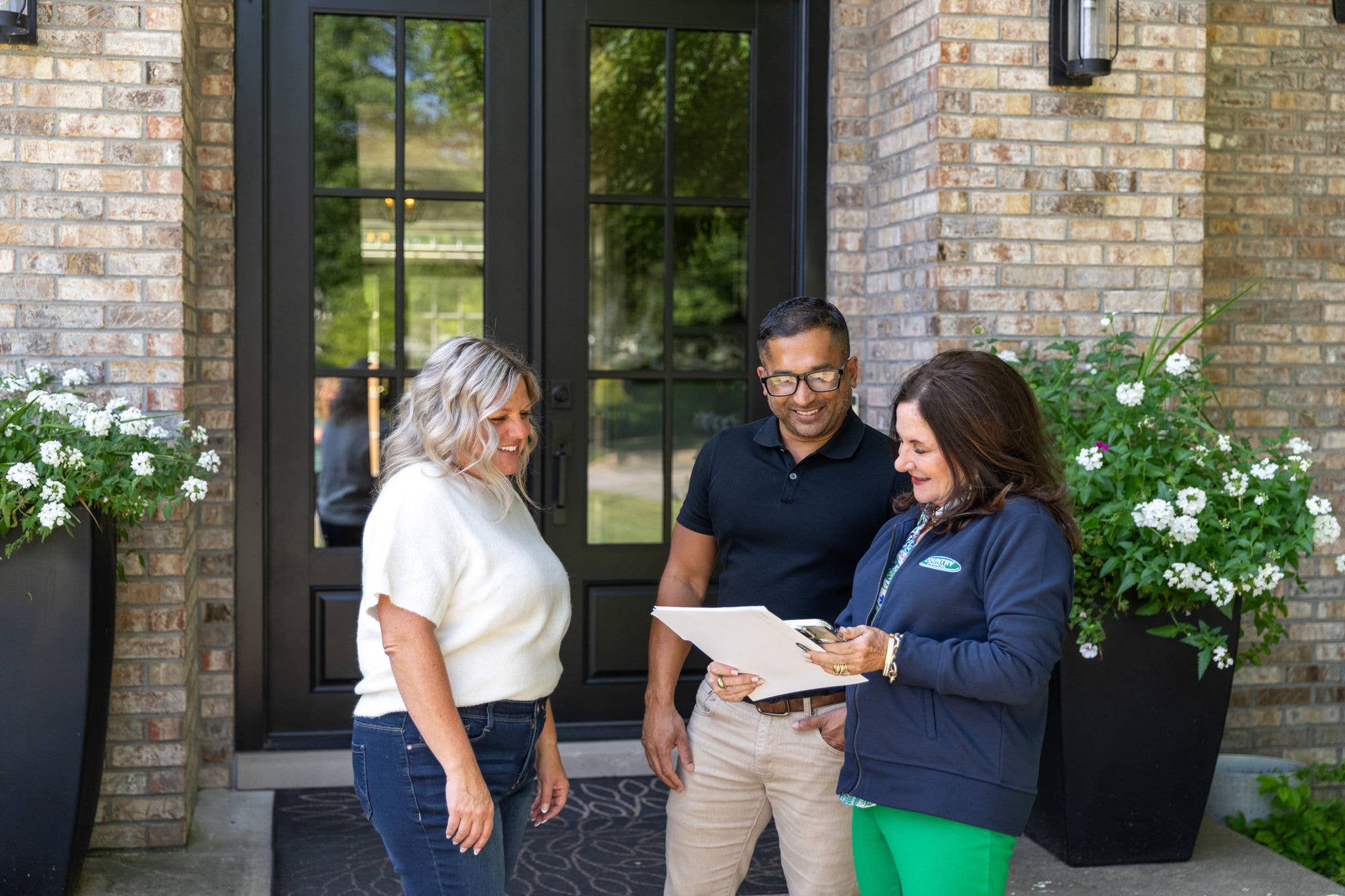 A COUNTRY Financial representative is reviewing paperwork with their clients in front of their home.