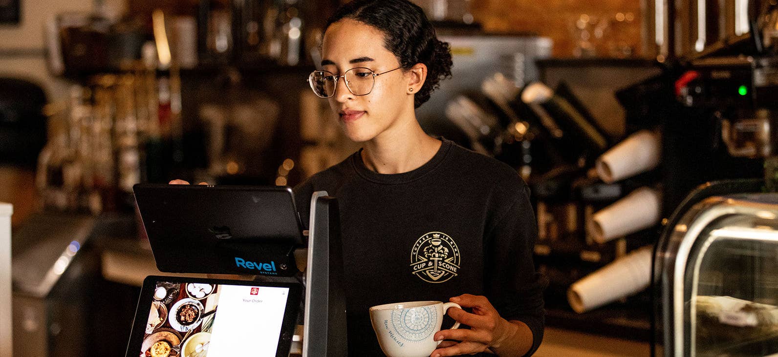 Barista holding coffee cup behind a register