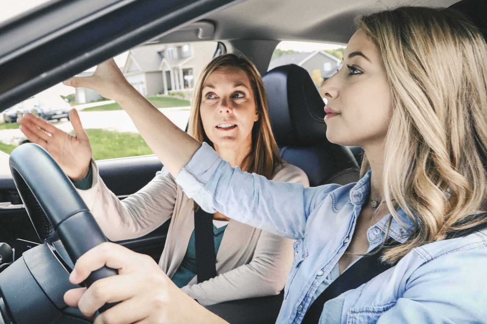 A blonde teen girl learning to drive with her mother.