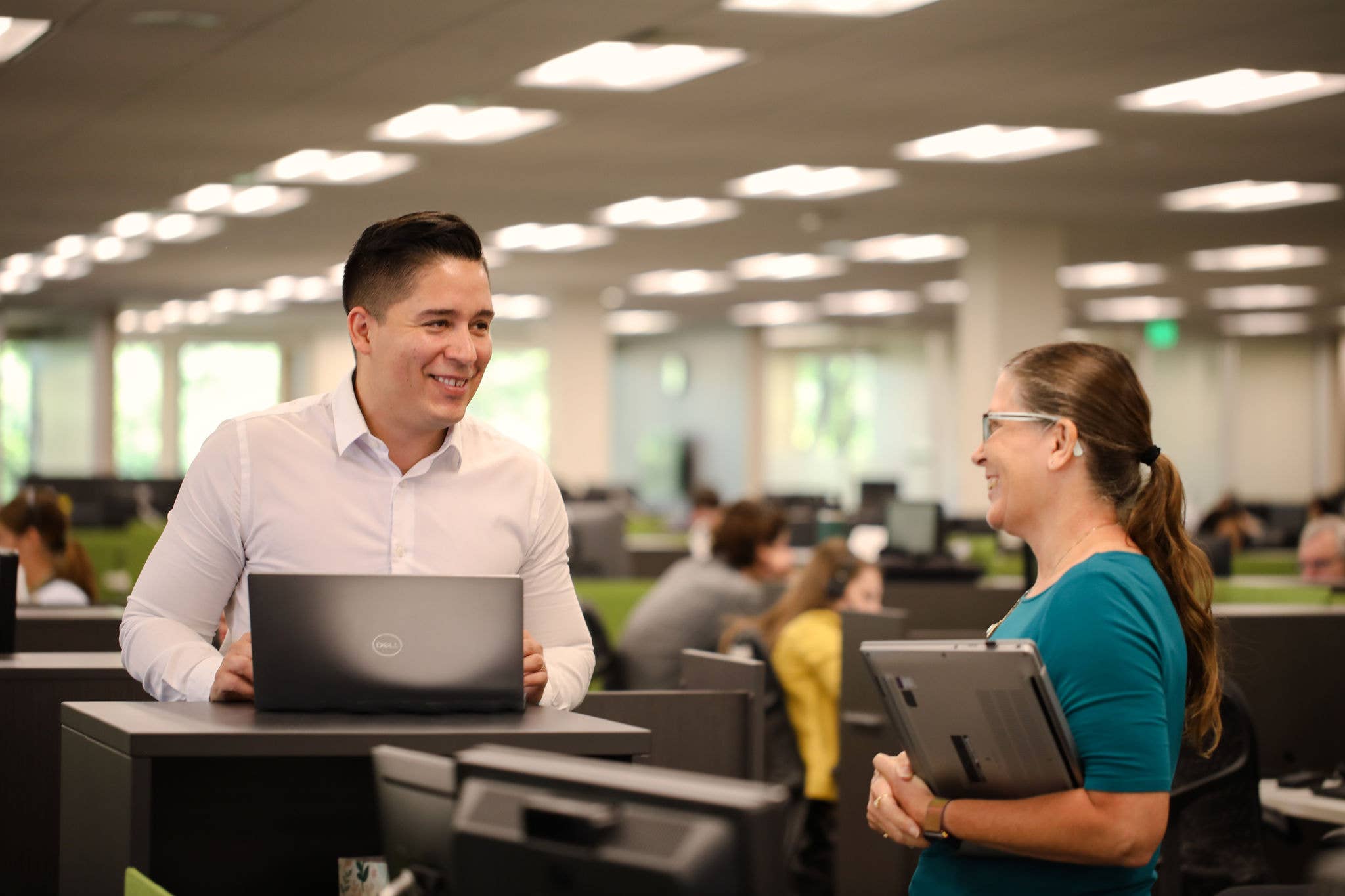 Two employees holding laptops talking in an office