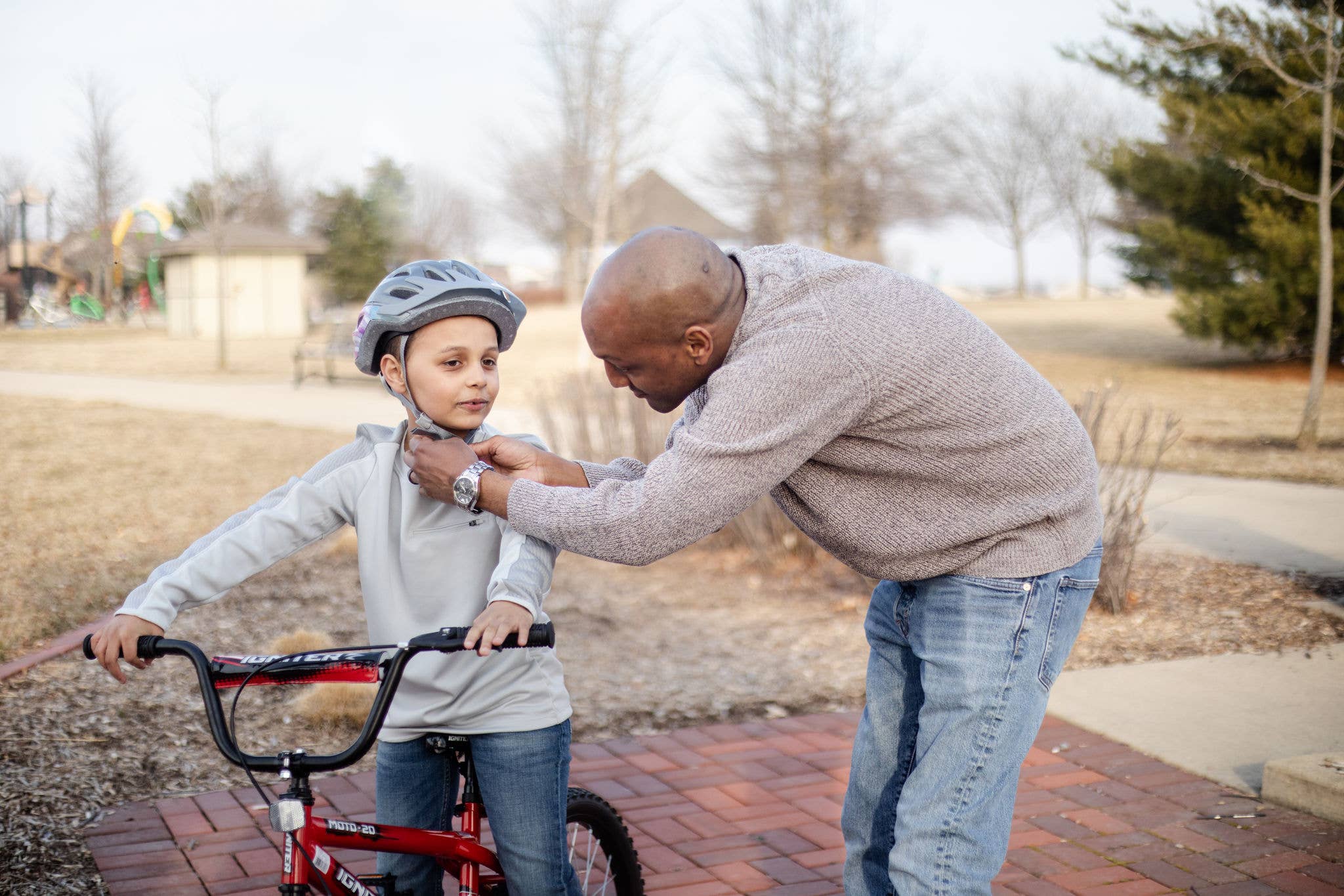 Father securing helmet on his young son who is sitting on a bike.