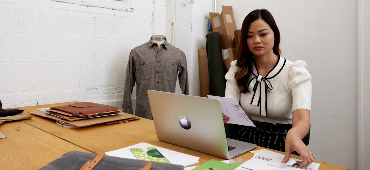 Business owner reviewing documents and using laptop at desk