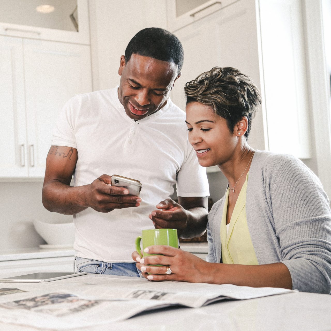 Couple looking at devices and news paper in kitchen drinking coffee