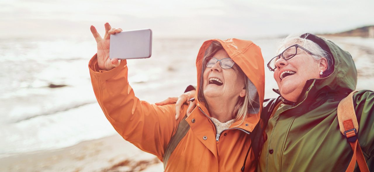 Two smiling female seniors taking a selfie picture on the beach