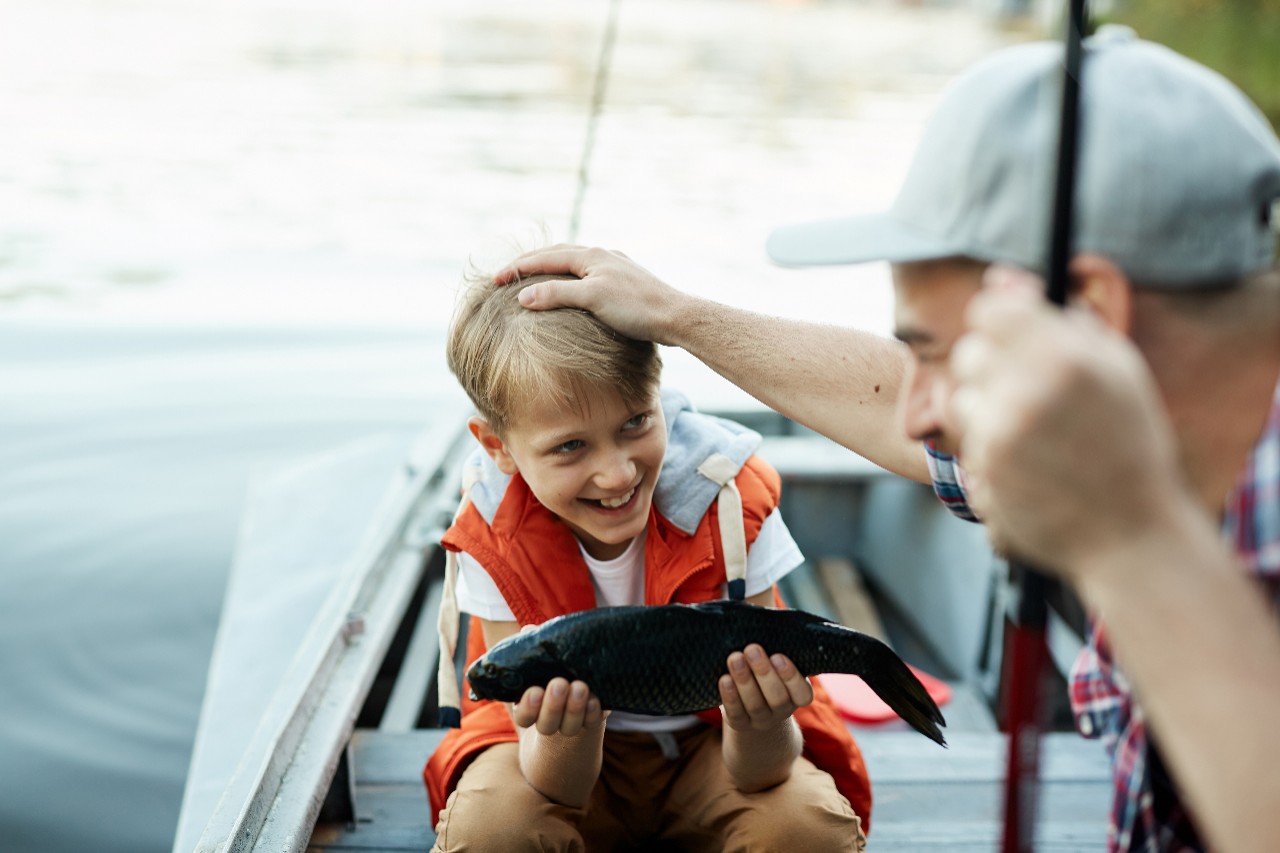 Happy boy holding big fish, and showing it to his father, while they are on the boat