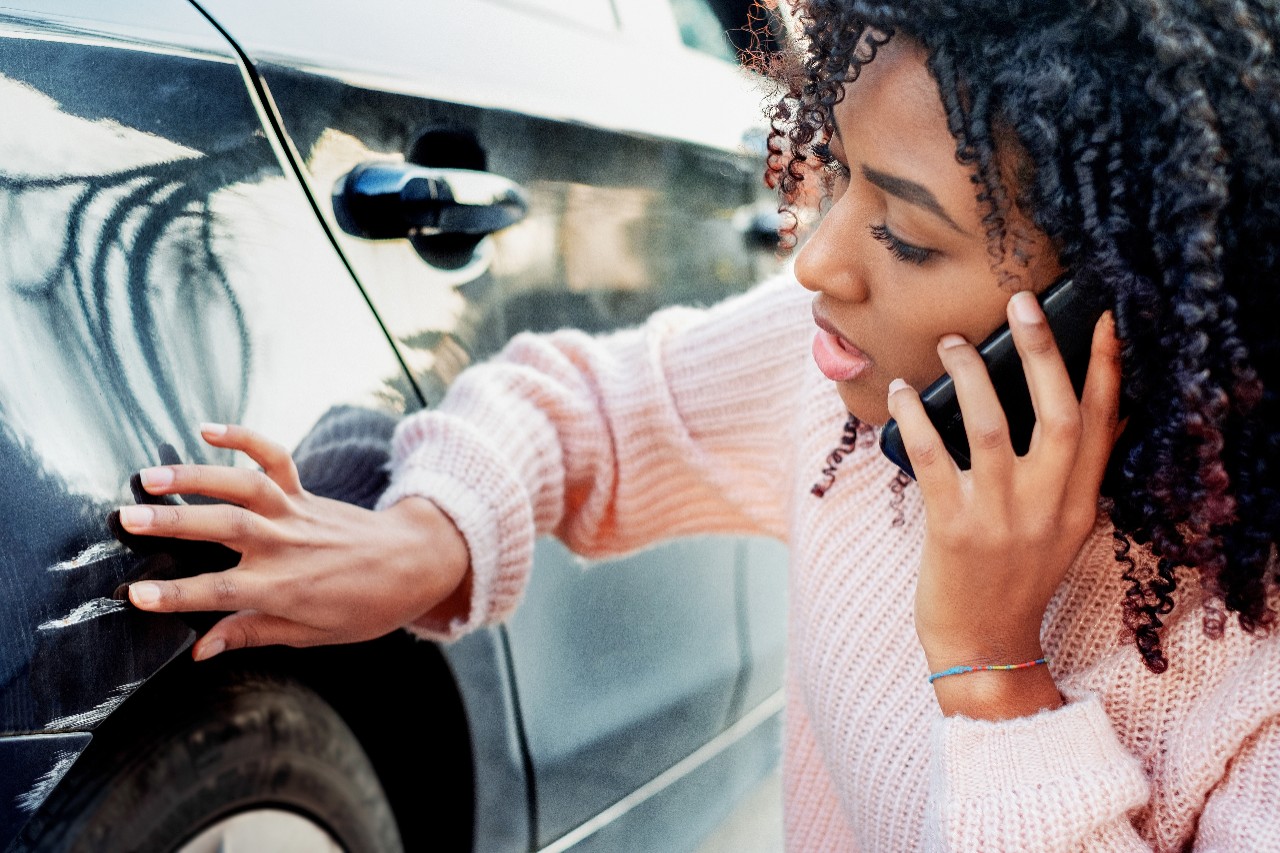 Black woman feeling sad after scratching car bodywork