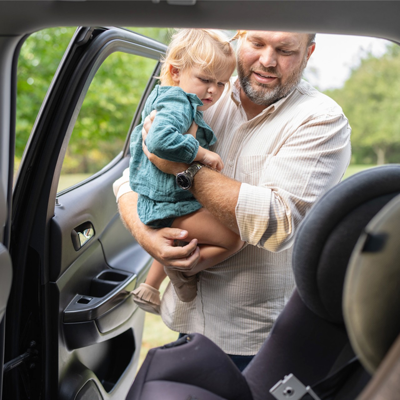 Dad loading child into rear car seat.