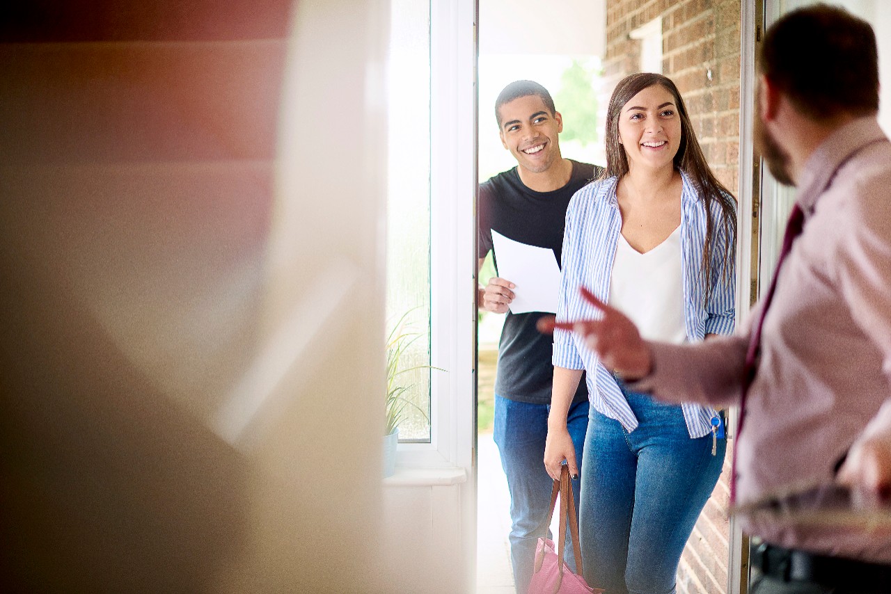 a young couple view a property guided by an estate agent. They are standing in the hallway of house and chatting about the paperwork that they are holding .