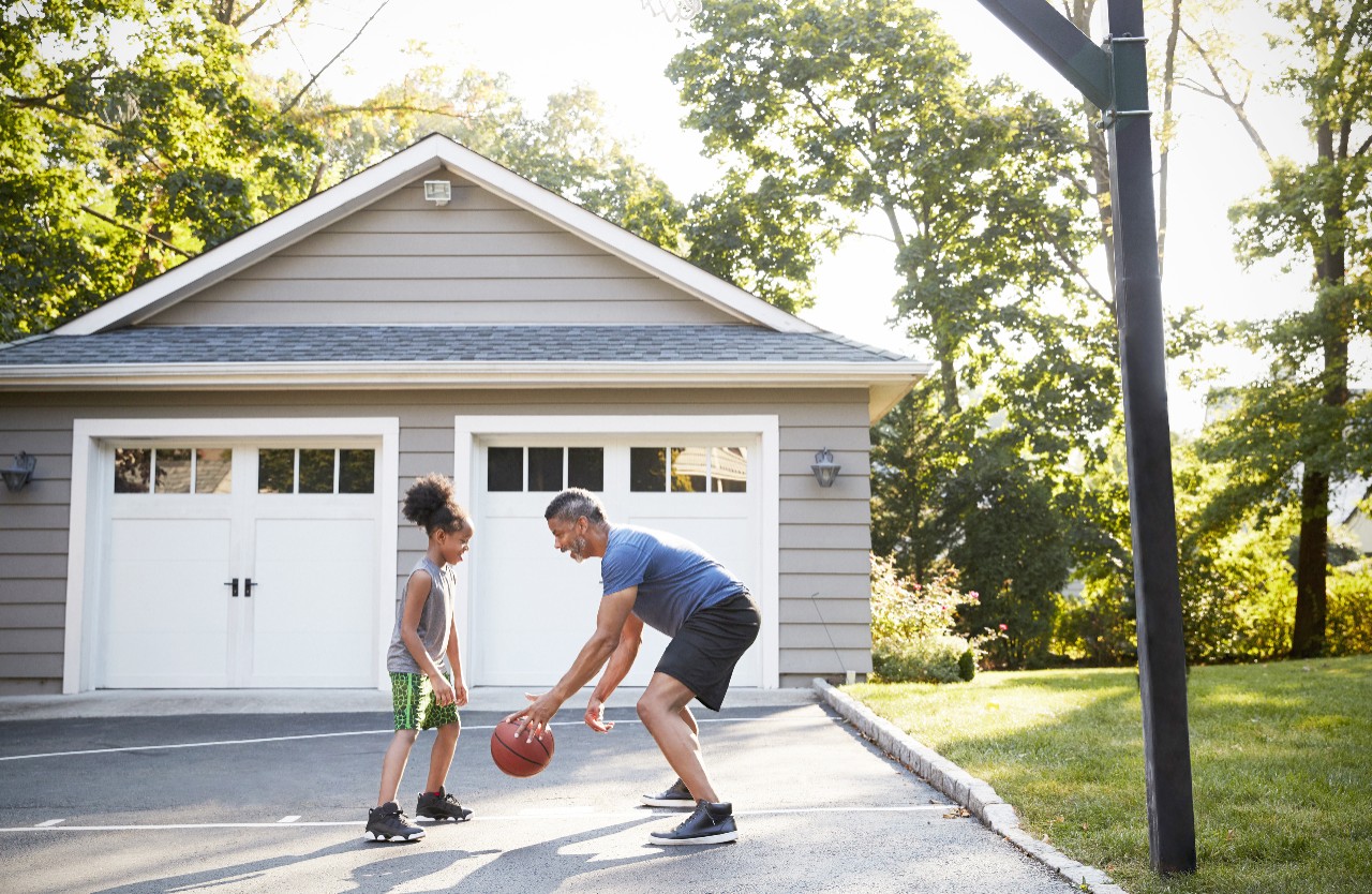 Father And Son Playing Basketball On Driveway At Home