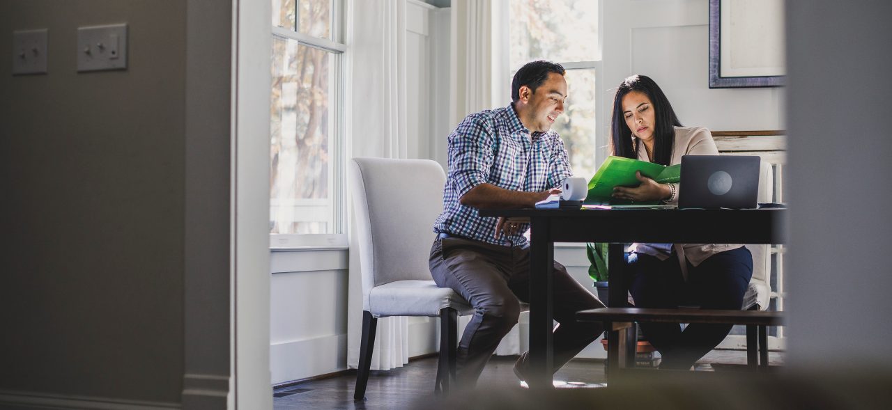 Couple sitting at dining table reviewing expenses with paper and computer