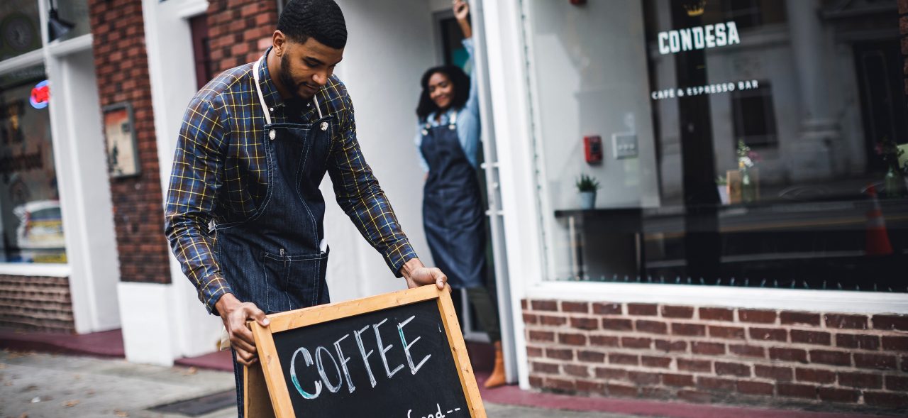 Business owner and worker setting up sign in front of coffeehouse 