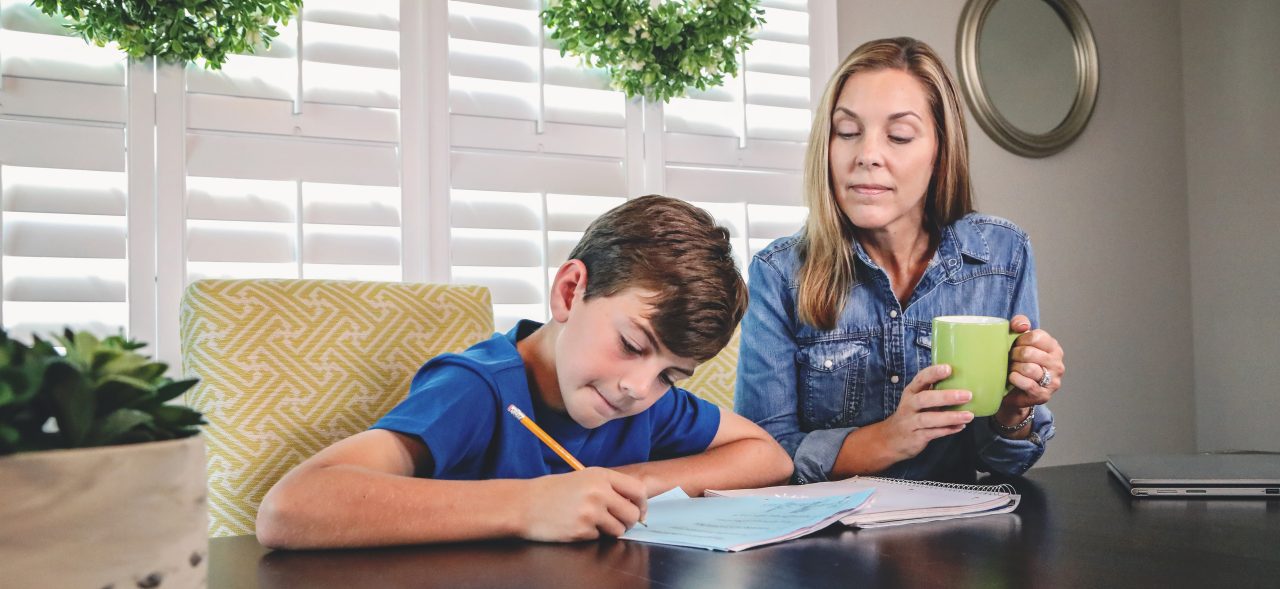 Mother helping son with homework sitting at kitchen table
