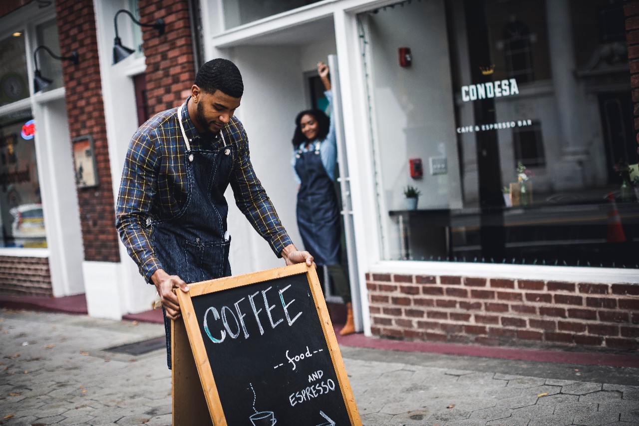 Business owner and worker setting up sign in front of coffeehouse 