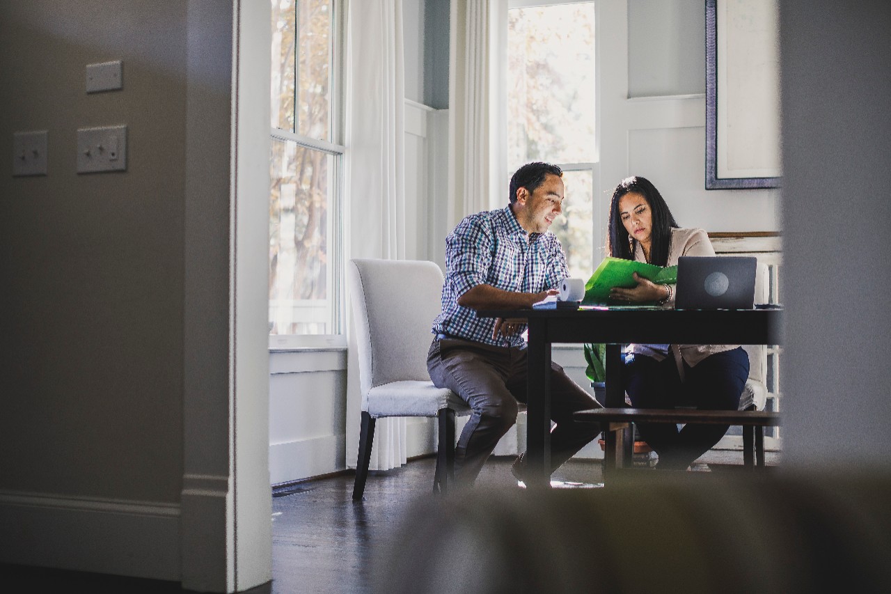 Couple sitting at dining table reviewing expenses with paper and computer