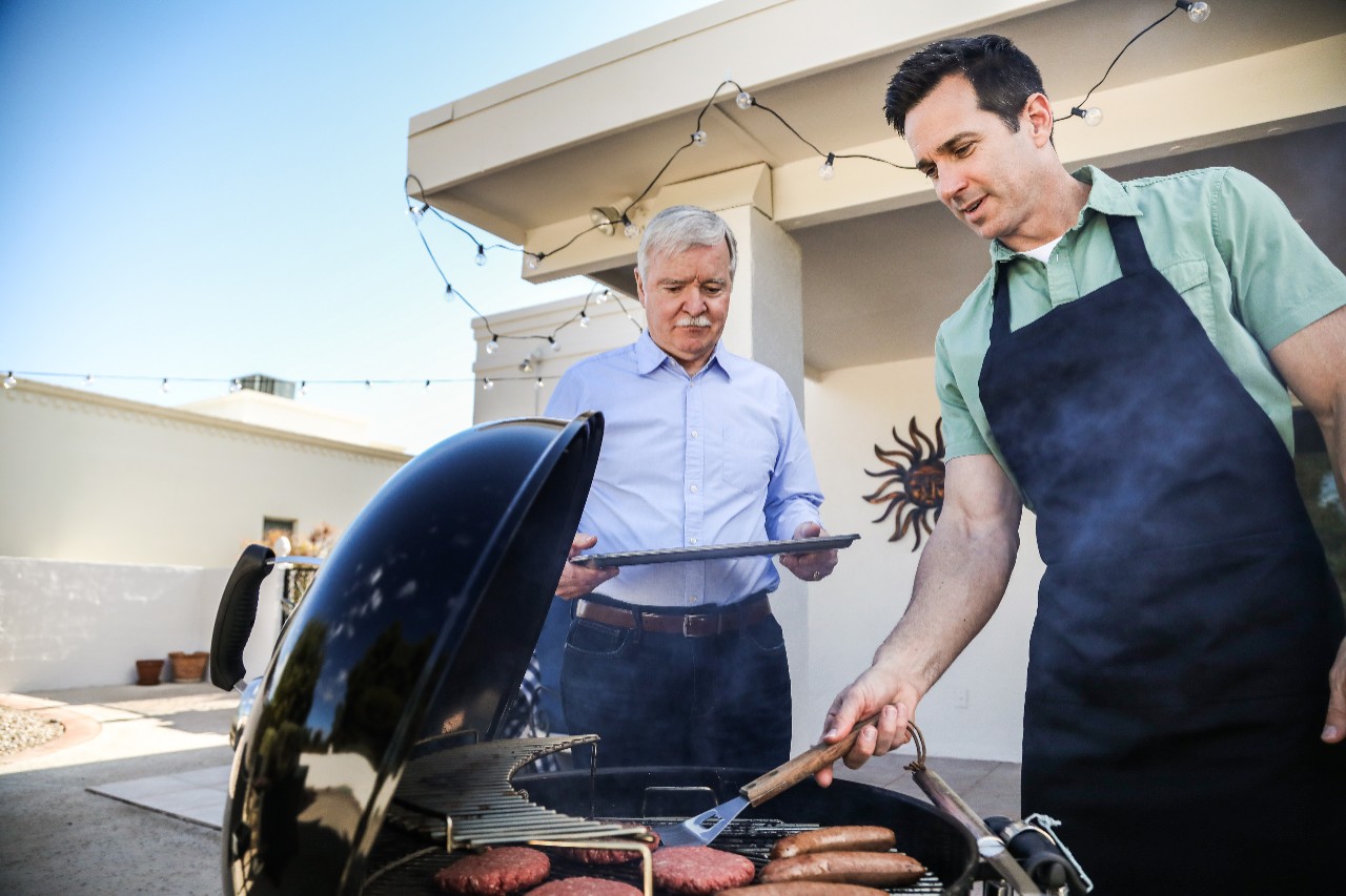 Senior father and adult son grilling on porch