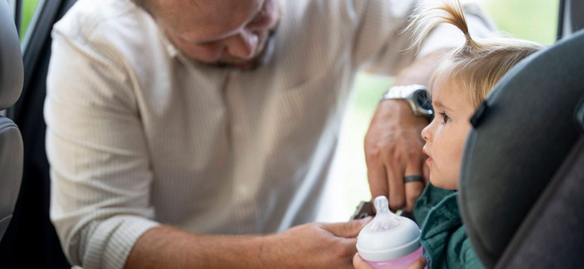 father buckling daughter in car seat