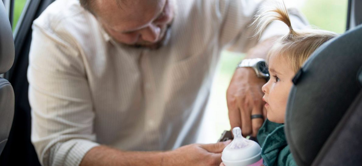 father buckling daughter in car seat