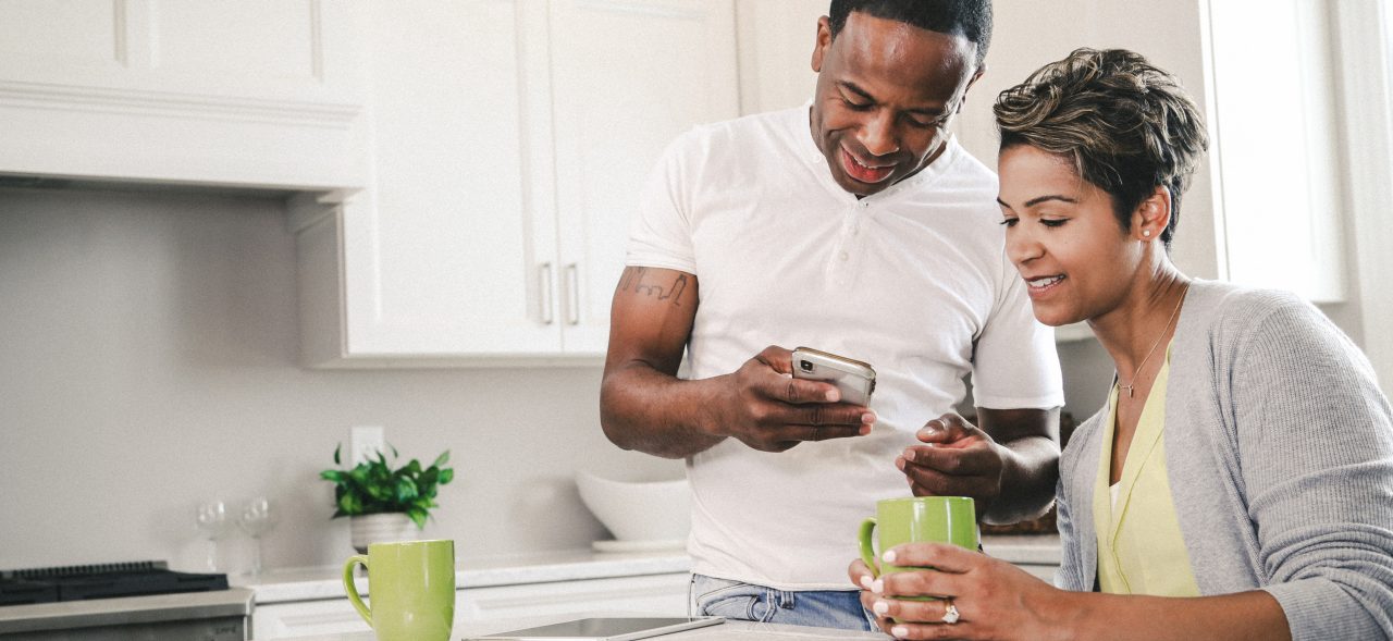 Couple looking at devices and news paper in kitchen drinking coffee