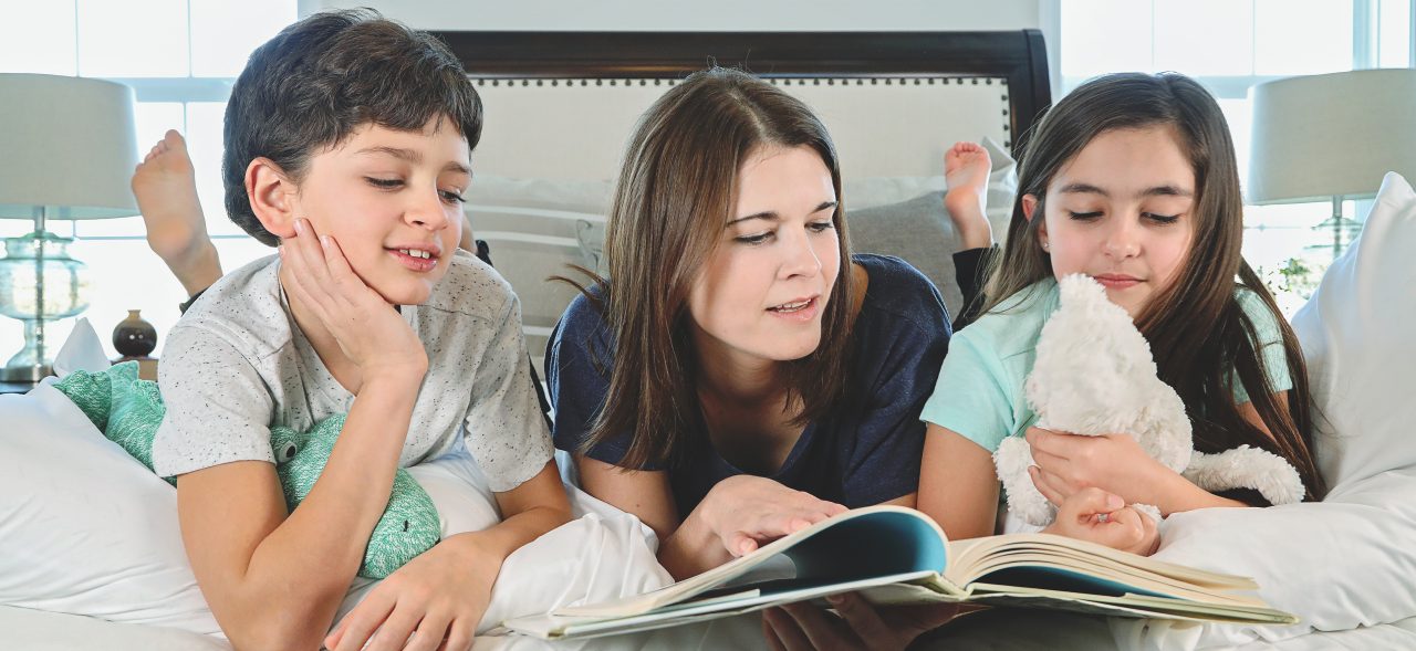 Mother reading bedtime story to two children laying in bed