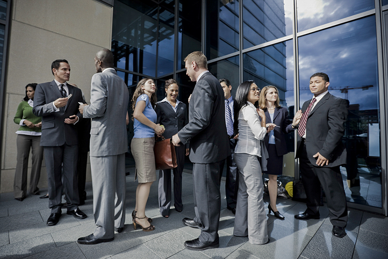 Outdoors business meeting in front of modern building exterior, talking and exchanging business cards.
