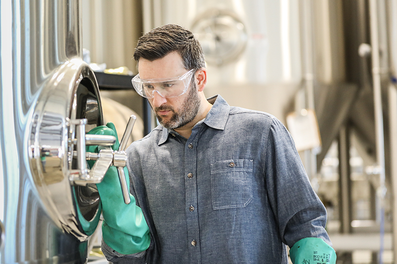 Brewery worker next to fermentation vessels