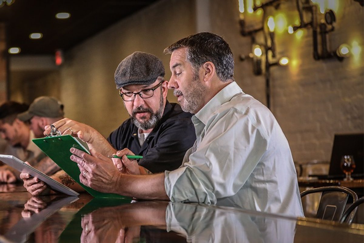 Insurance representative looking at clipboard with man at counter