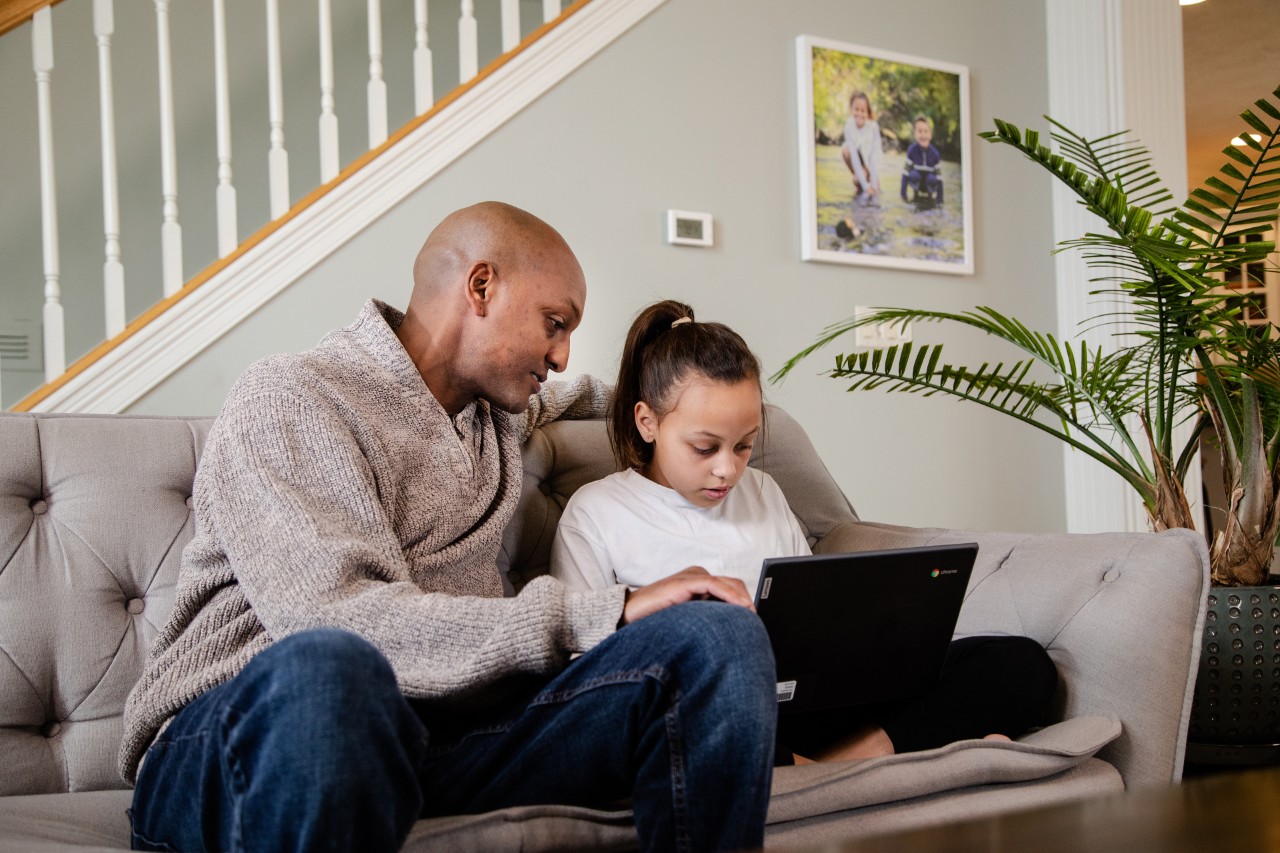 Father helping daughter with laptop on living room couch