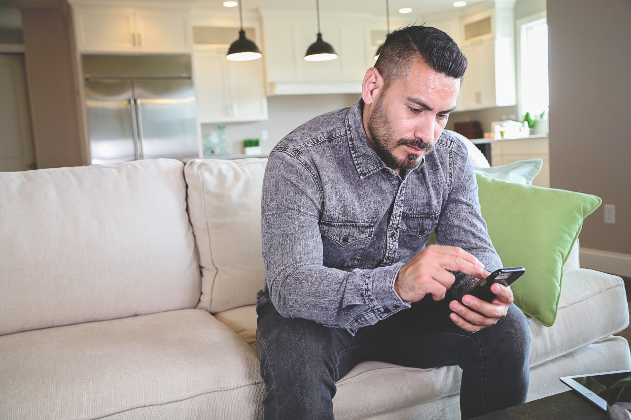 Hispanic male sitting on couch looking at phone