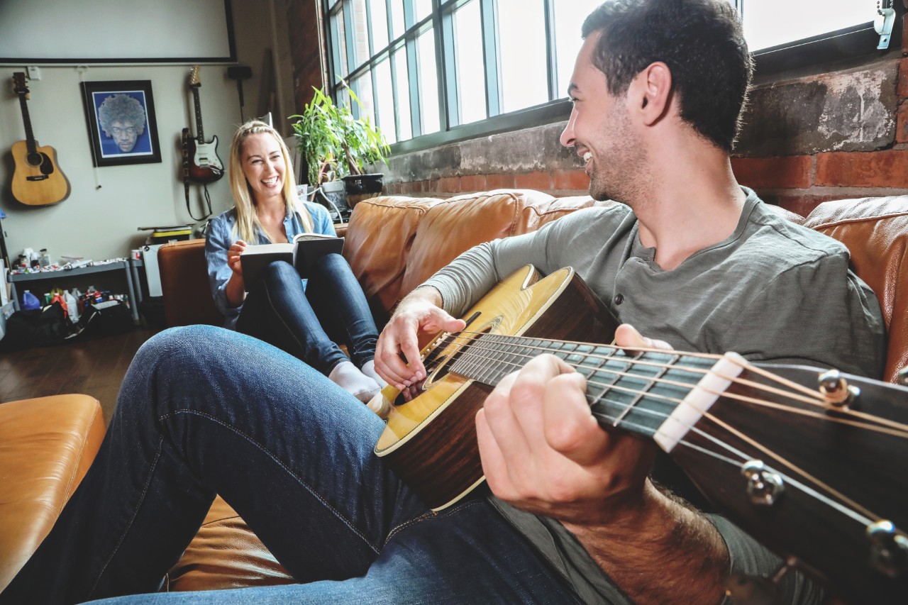 Male playing guitar on couch with female reading a book