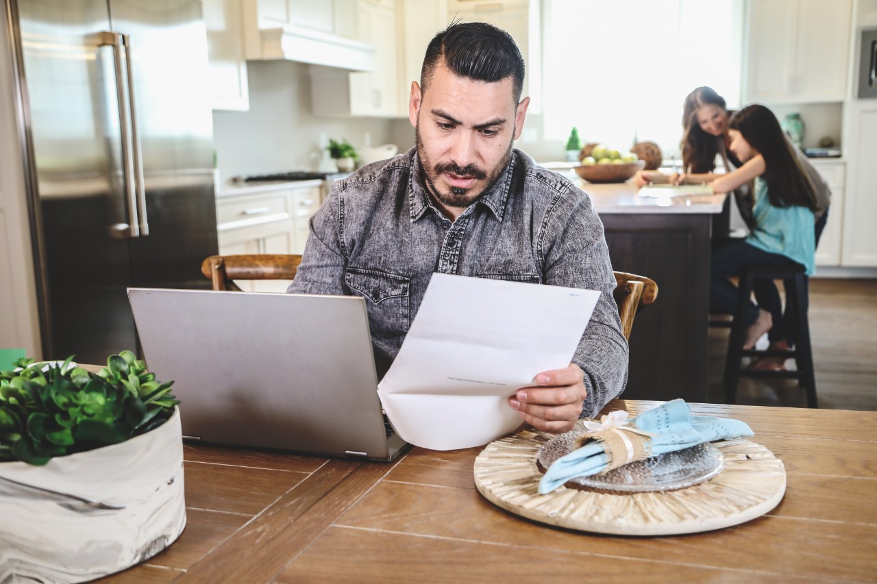 Hispanic male sitting at table with computer and paperwork