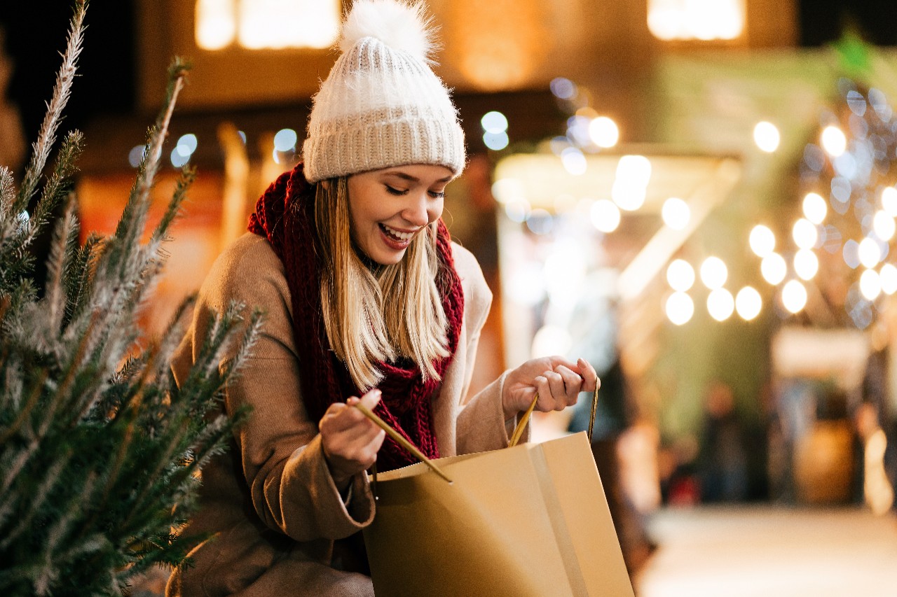 Happy young woman choosing holiday present and tree at market
