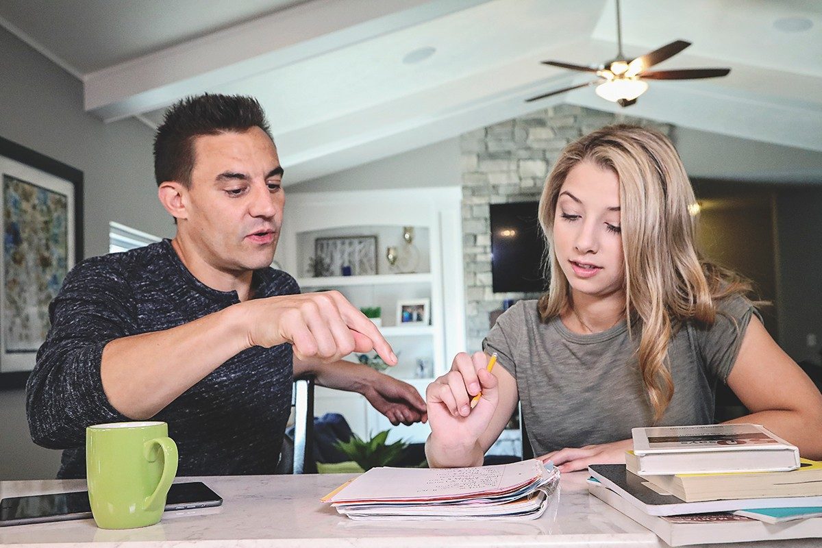 Father helping daughter with homework at kitchen table