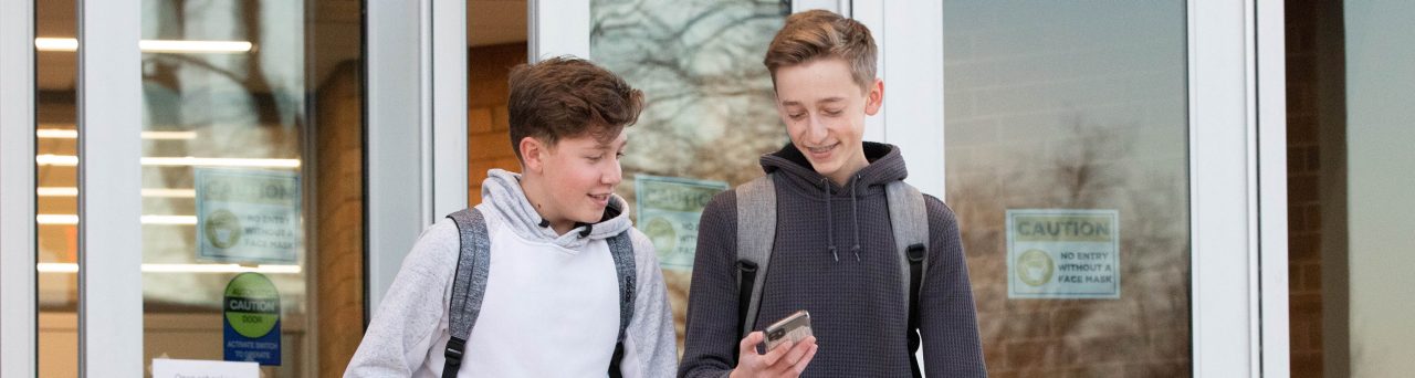 Two boys walking out of school looking at phone